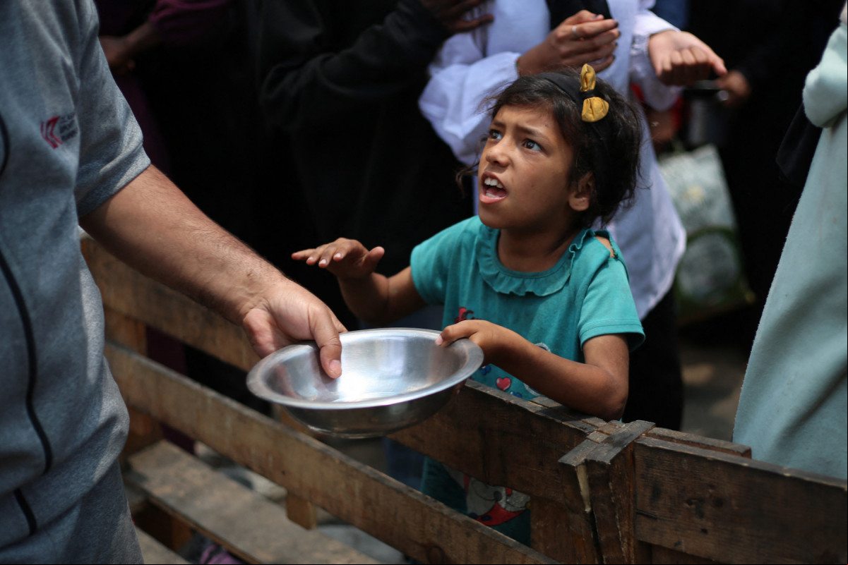 Uma menina palestina segura uma a vazia em um ponto de distribuição de refeições quentes em Nuseirat, no centro da Faixa de Gaza