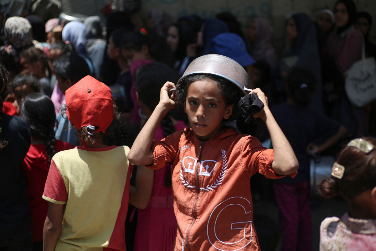 Uma menina palestina cobre a cabeça com uma a vazia enquanto espera em um ponto de distribuição de refeições quentes em Nuseirat, no centro da Faixa de Gaza
